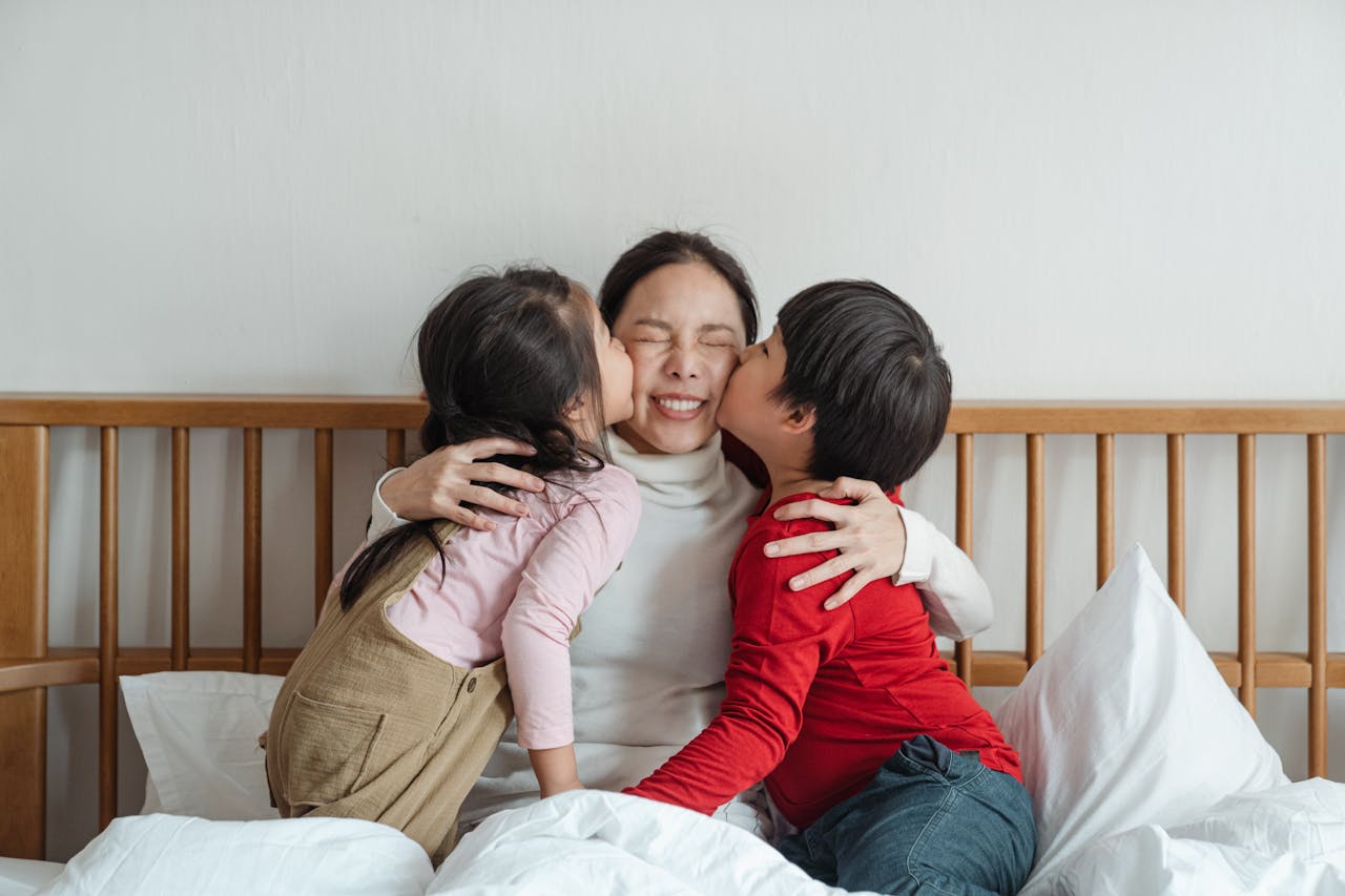 Happy mother embraced by children on bed, sharing joyful bonding moments indoors.