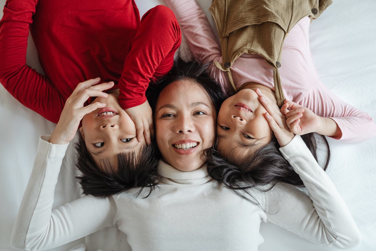 Mother and two children laughing and bonding while lying head to head on the bed at home.